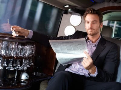 A man sitting in the back of a limo reading paper.
